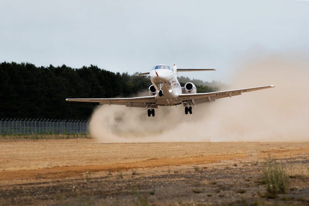 Plane landing on an unpaved airstrip stirring up dust.