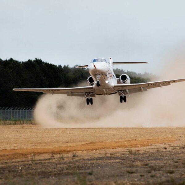 Plane landing on an unpaved airstrip stirring up dust.