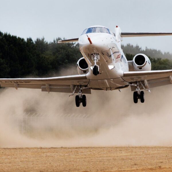 Plane landing on an unpaved airstrip stirring up dust.